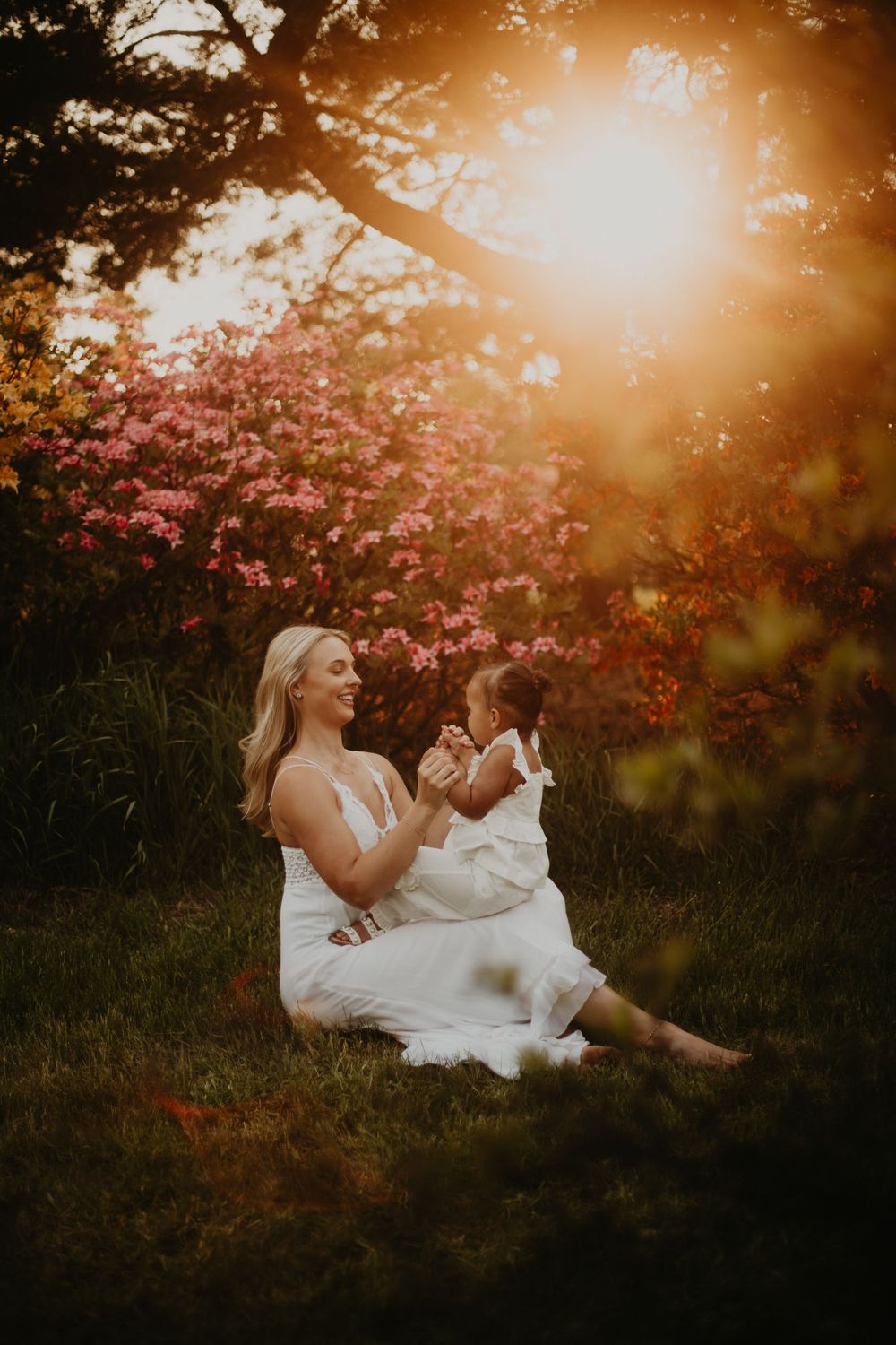 A dreamy golden sunset photoshoot in a flower garden with warm glowing light filtering through trees and pink blooms.