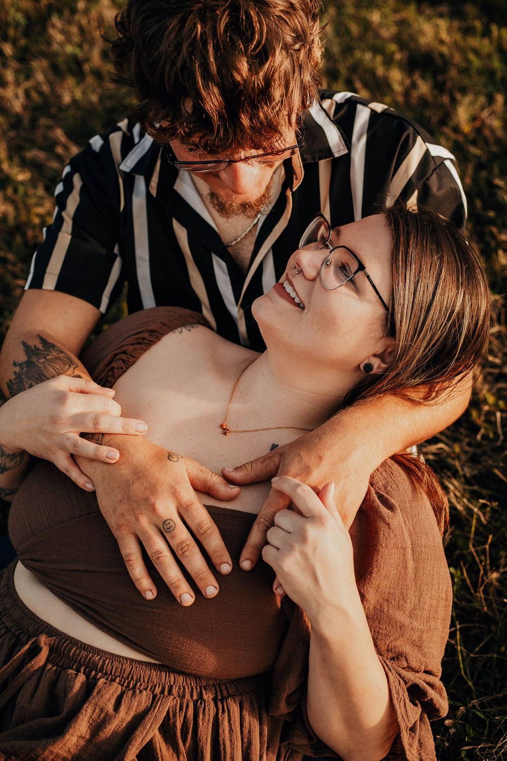 A couple embraces outdoors during golden hour, sharing a tender moment while sitting on the ground.