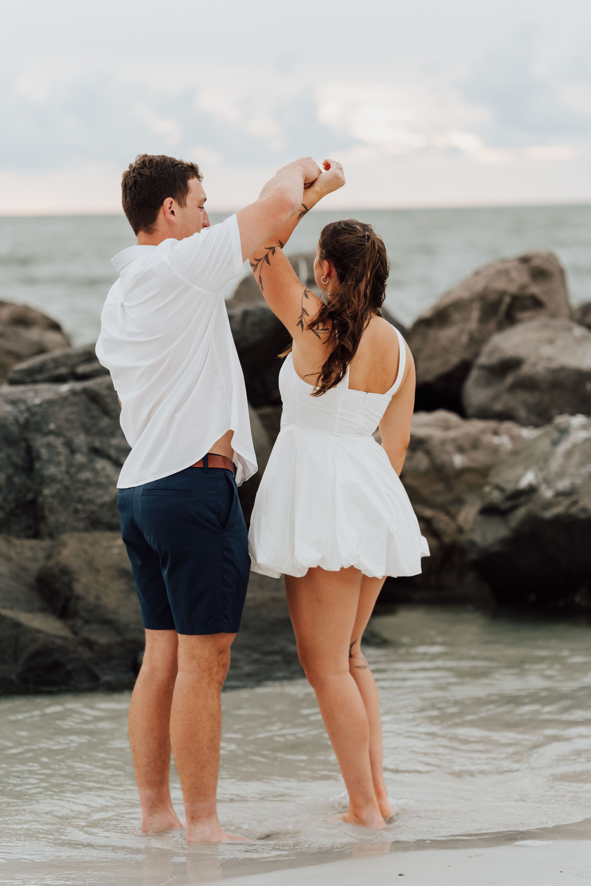 Coastal engagement photoshoot in St. Pete Beach featuring a couple in white and blue outfits near tropical palms.