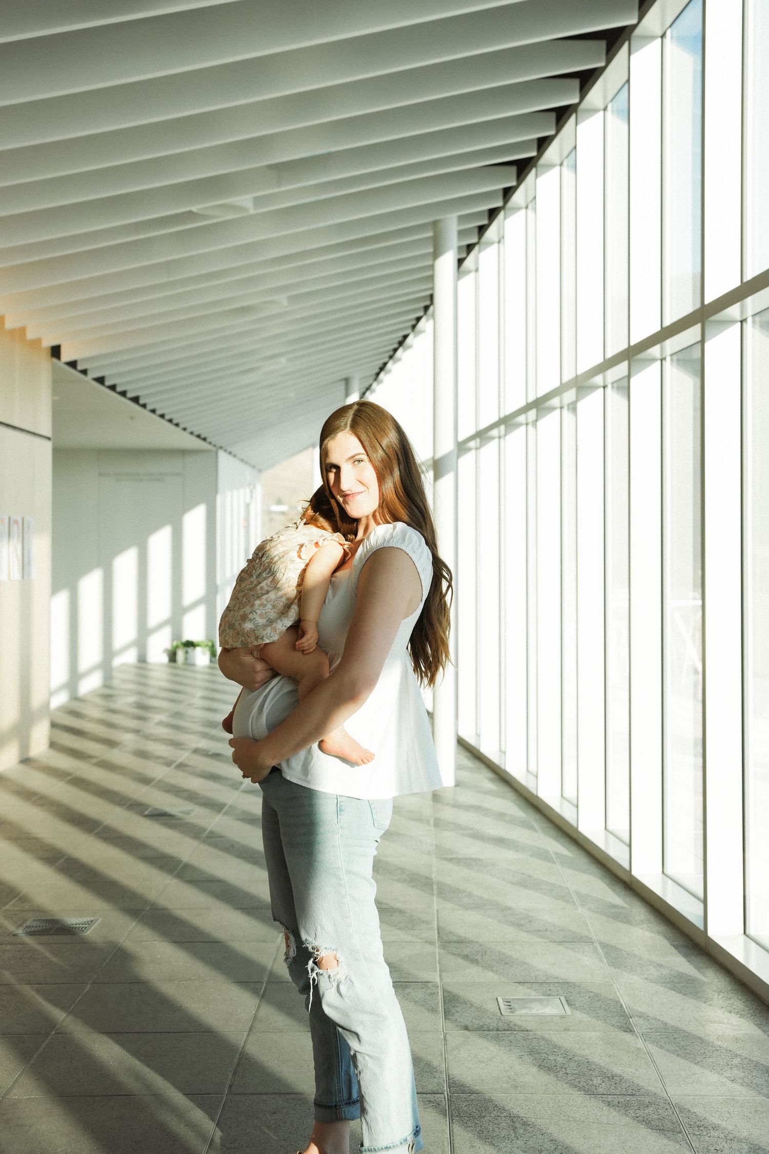 A series of maternity photos showing someone in a white top and jeans posing against a modern building exterior.
