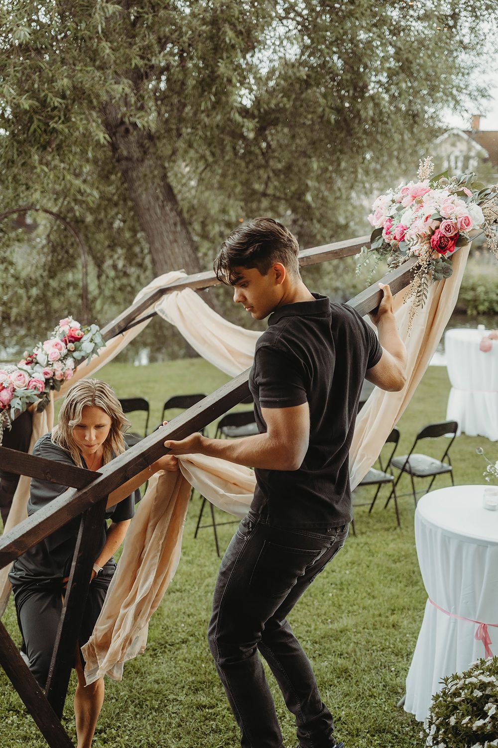 Bröllopsbågedekorerad med blommor och skirt tyg bärs in från trädgården på grund av regn under vigsel på Ångbageriet i Borensberg.