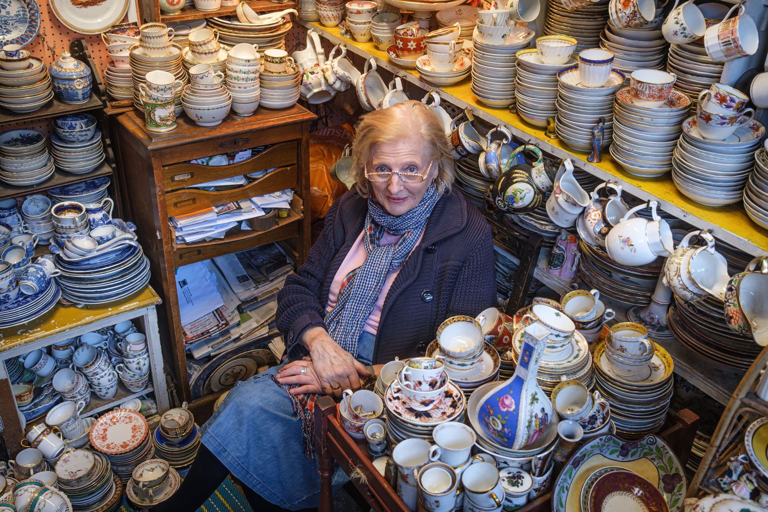 A vast collection of vintage teapots, cups, and saucers displayed on wooden shelves in an antique shop in Camden Passage.