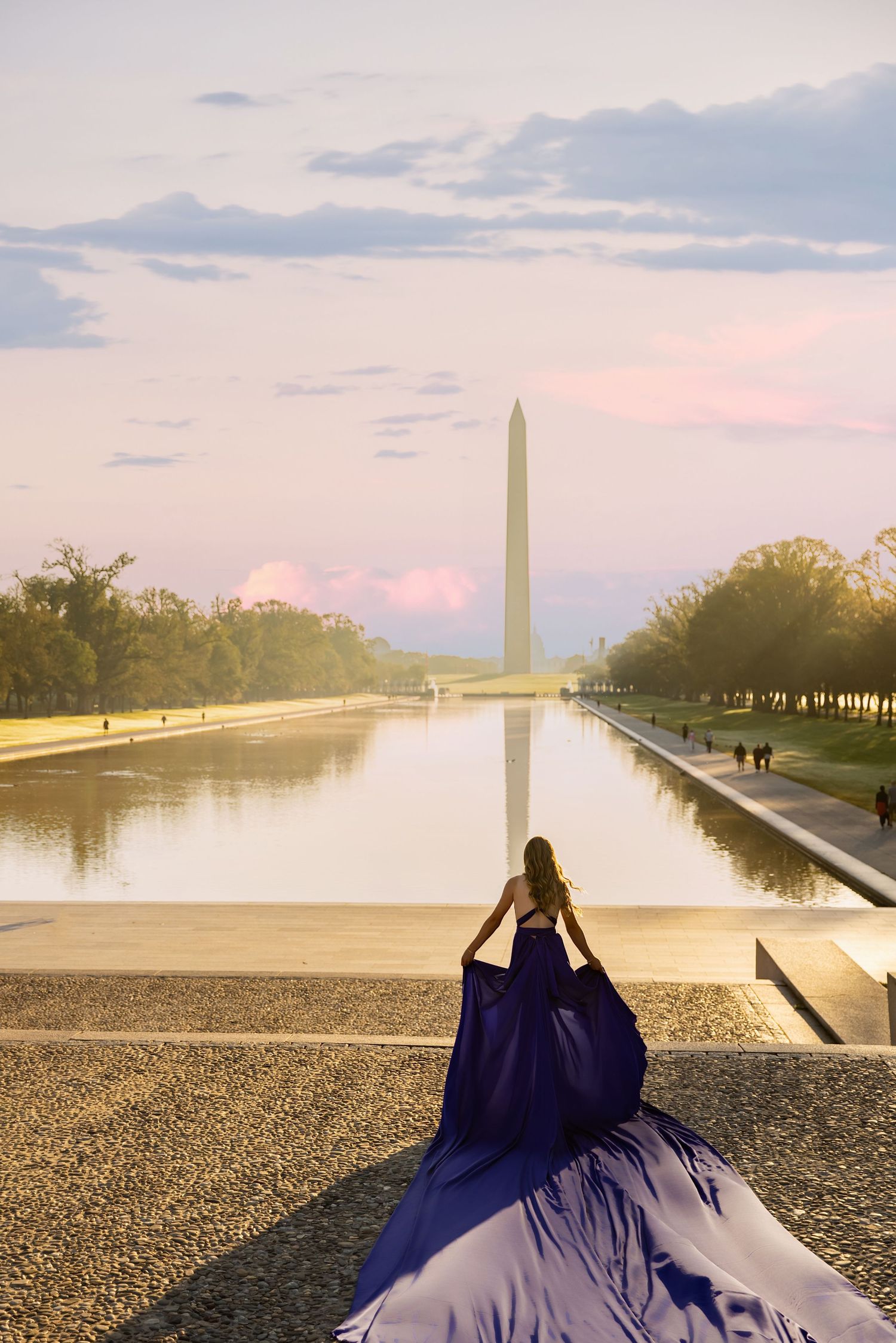 A figure in a flowing navy blue gown stands before the reflecting pool at the Washington Monument during sunset. My Flying Dress Photos
