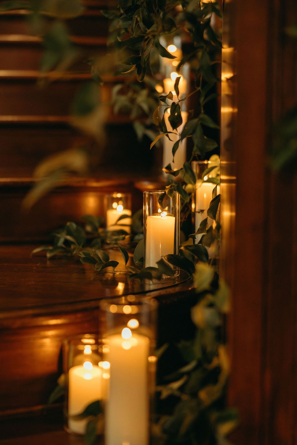 White pillar candles and greenery line wooden stairs creating a romantic, warm ambiance in dim lighting at Summerour Studio in Atlanta, GA