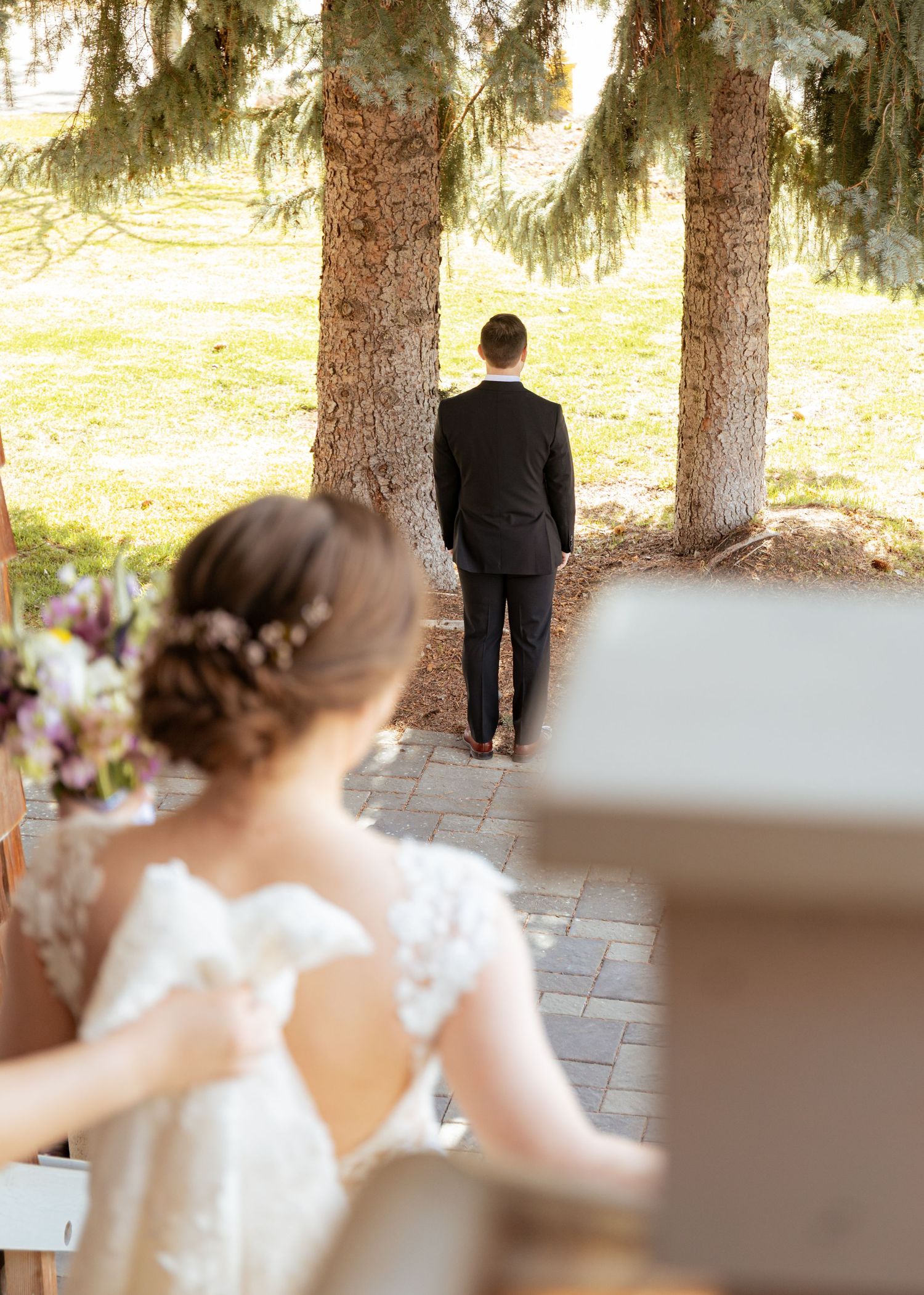 A wedding party walks along a stone path surrounded by evergreen trees during an outdoor ceremony.