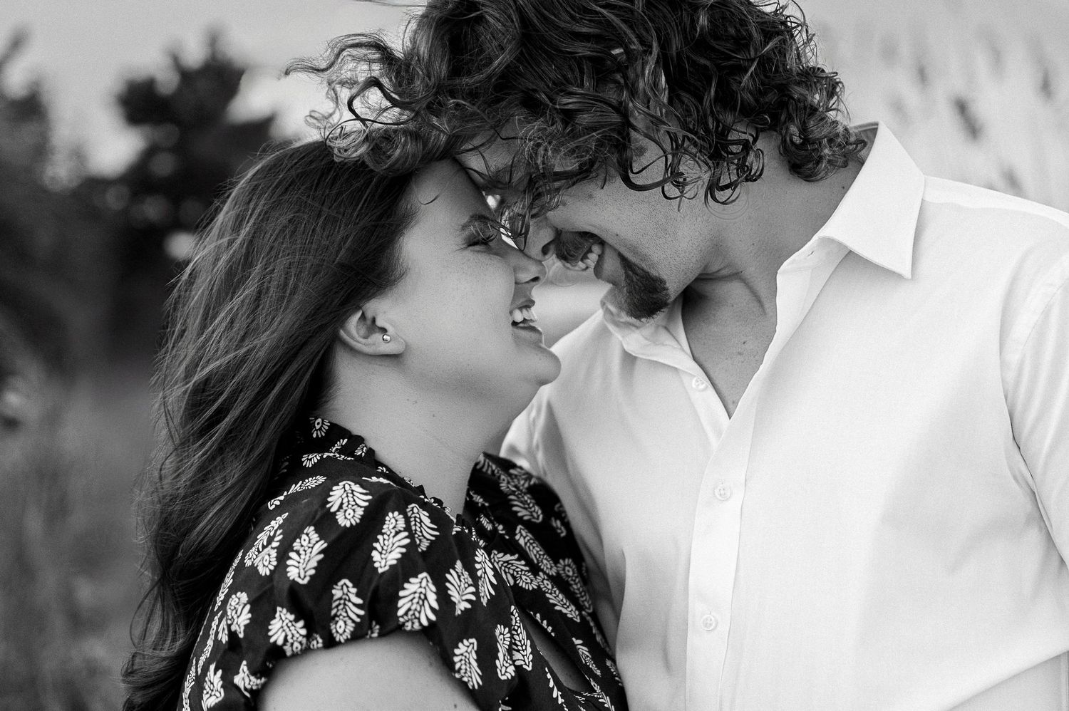 A romantic black and white portrait of a couple embracing on the beach with sea grass in view.
