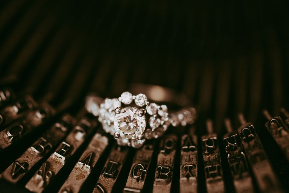 A sparkling diamond engagement ring rests on vintage typewriter keys in a moody, artistic macro shot.