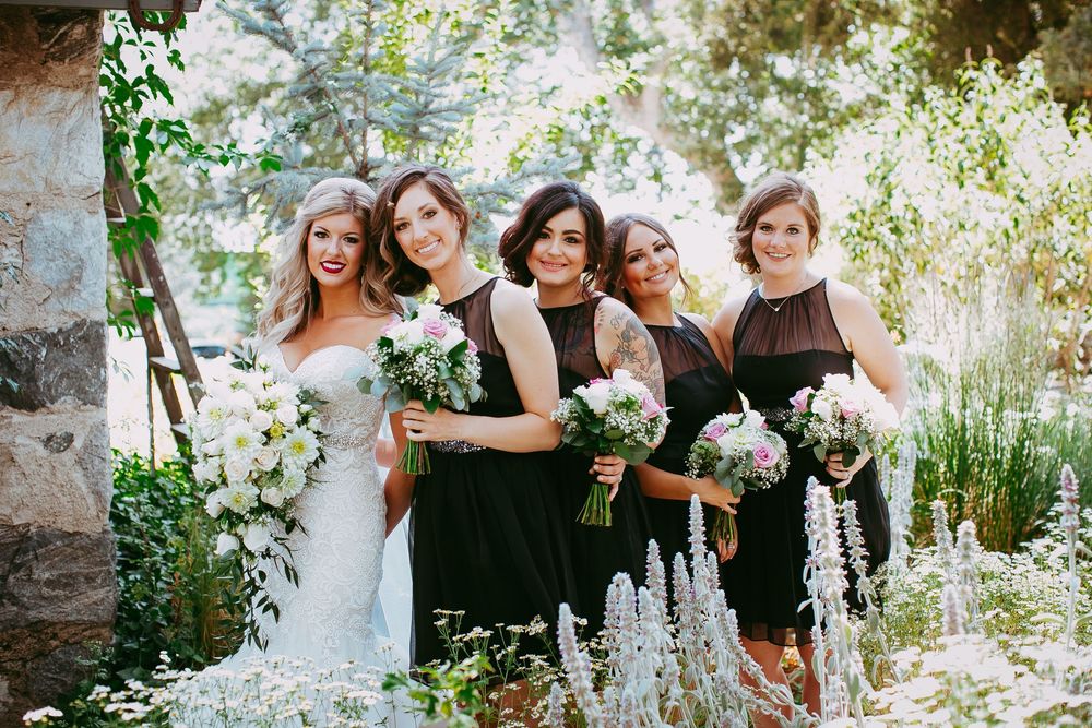 A group poses together in a garden setting wearing formal attire and holding white floral bouquets.