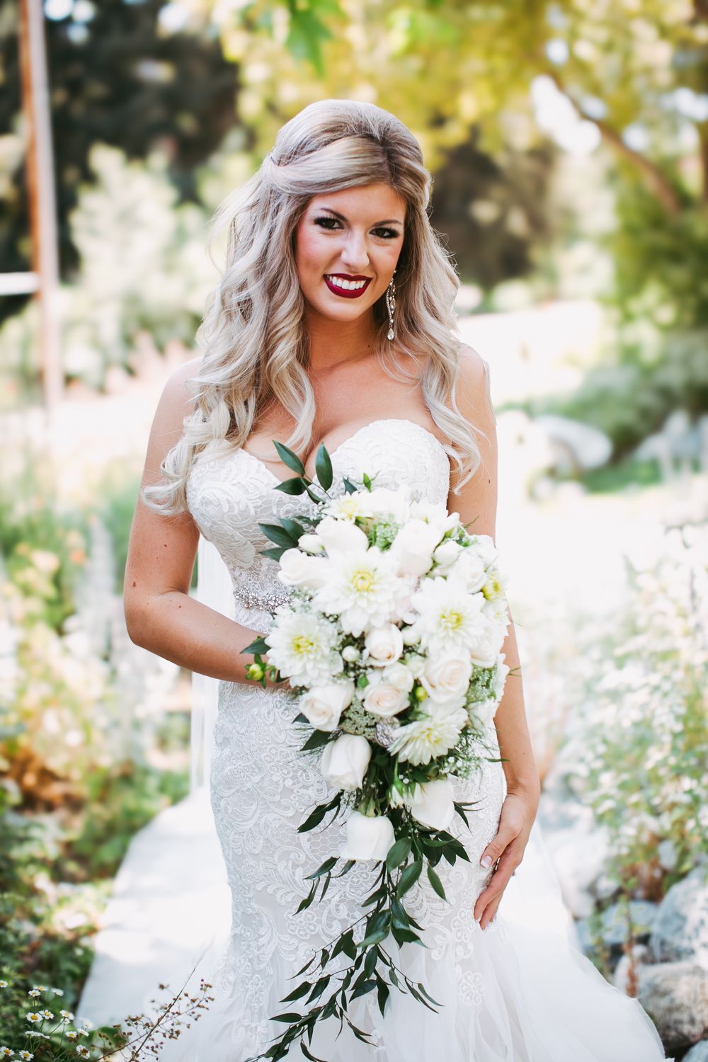 Beautiful white bridal bouquet with cascading flowers and greenery against a sunlit outdoor background.