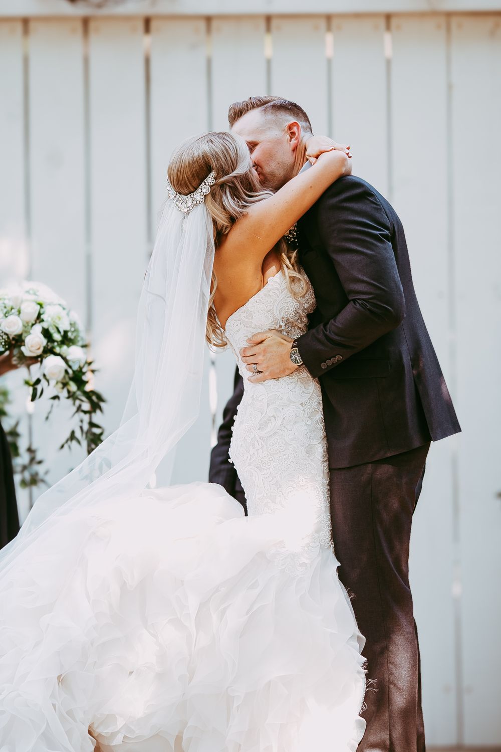 Romantic first dance moment captured against white barn doors at outdoor wedding venue.