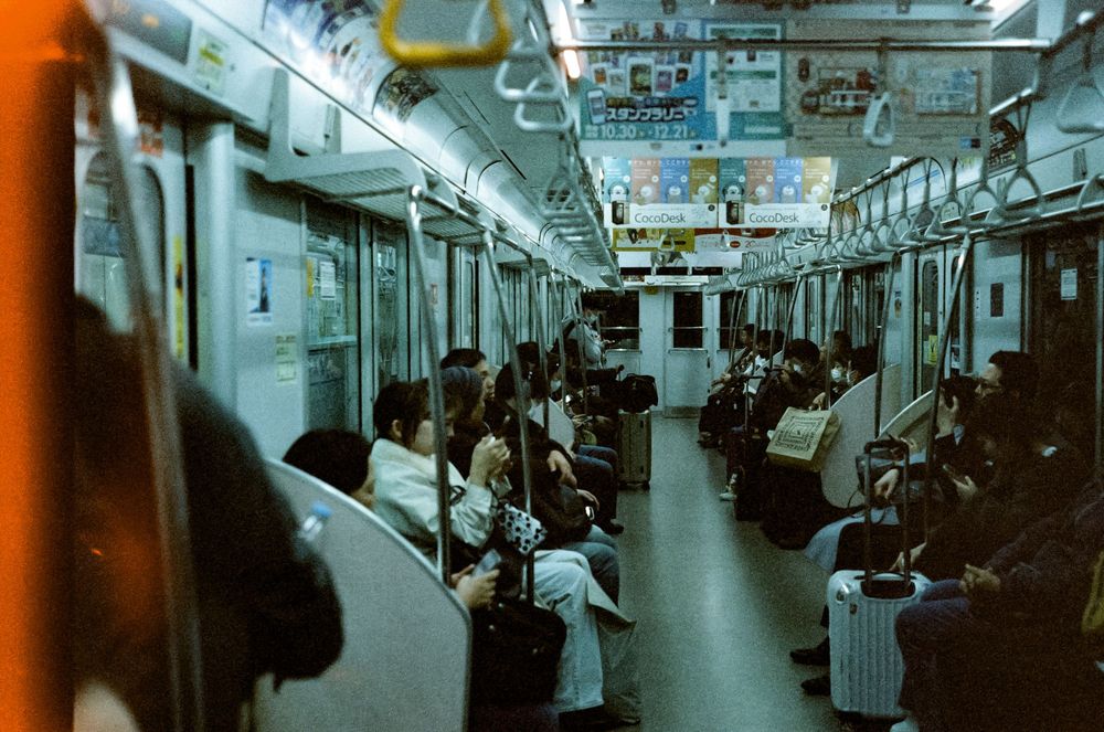 Interior view of a subway car with passengers sitting and standing along the length of the brightly lit carriage.