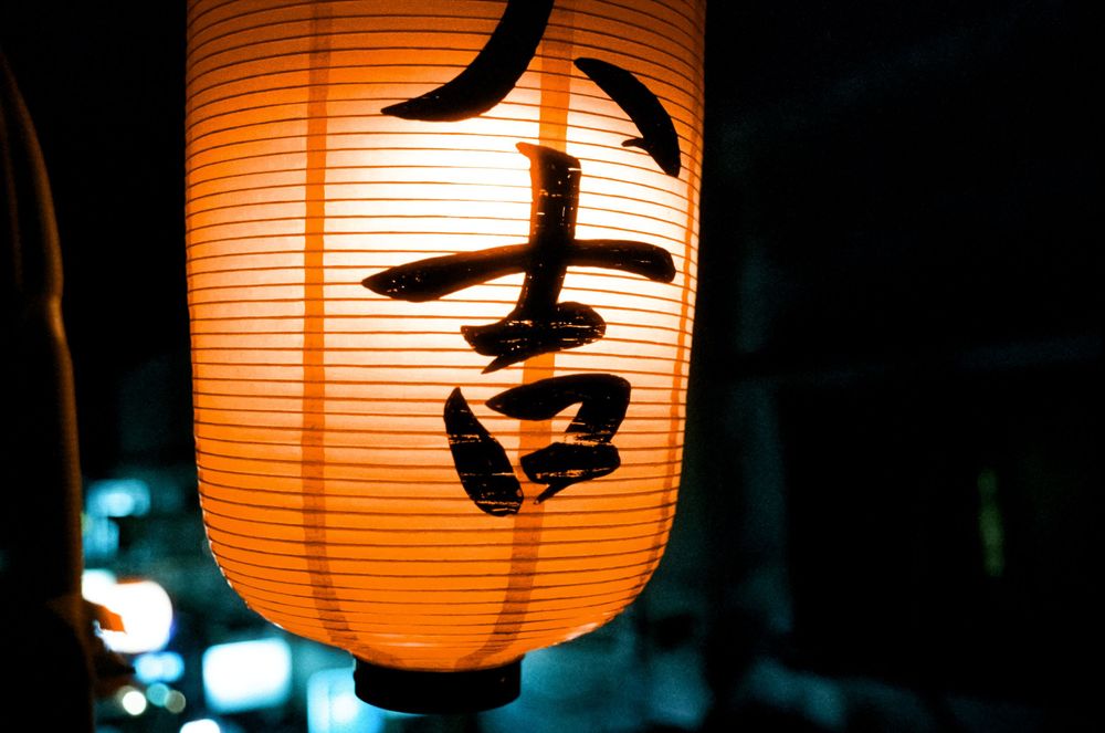 Orange paper lanterns glow warmly against a dark background creating atmospheric Japanese-style lighting.