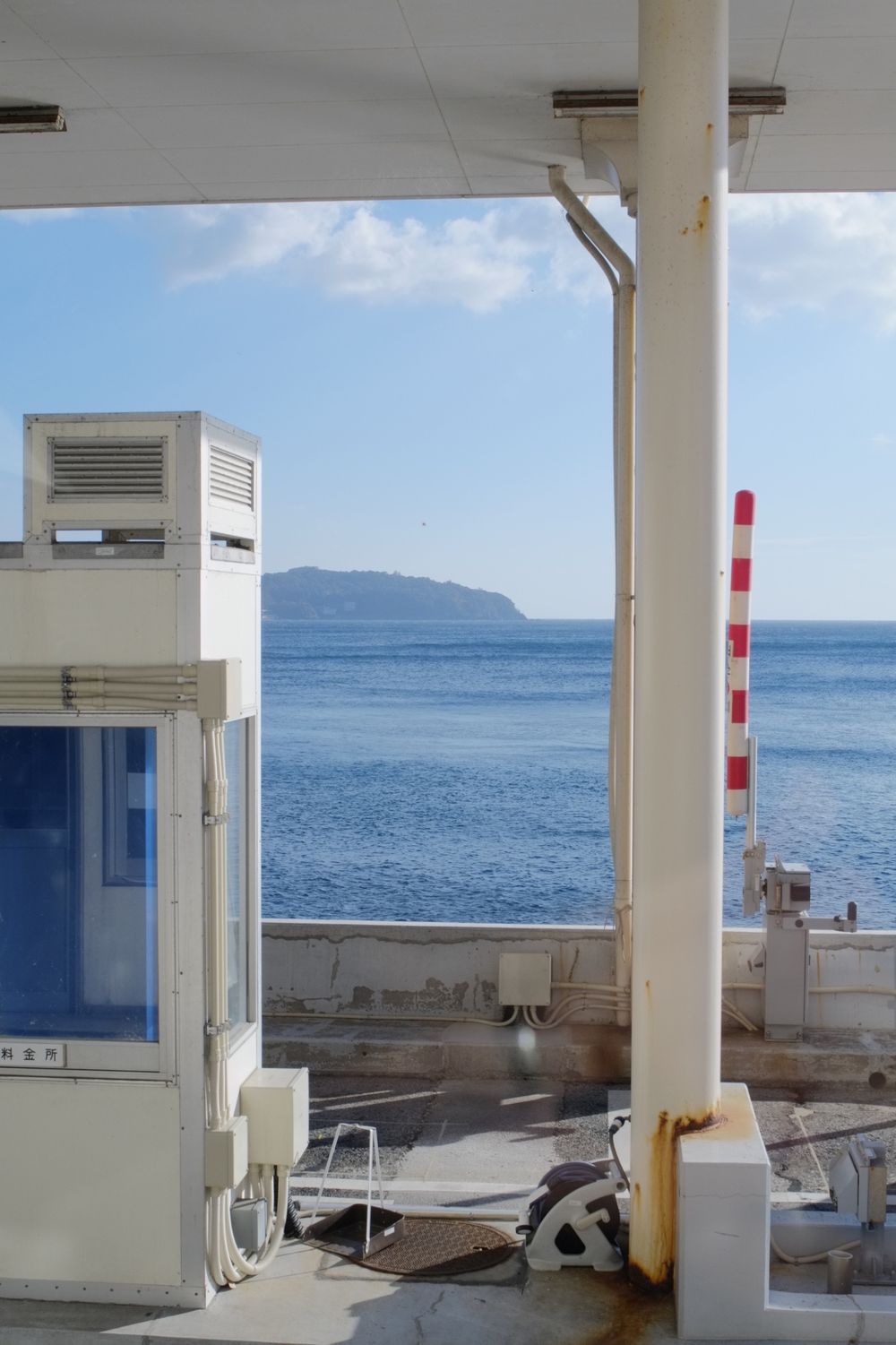 A series of white columns frame a scenic ocean view with mountains visible in the distance on a clear day.