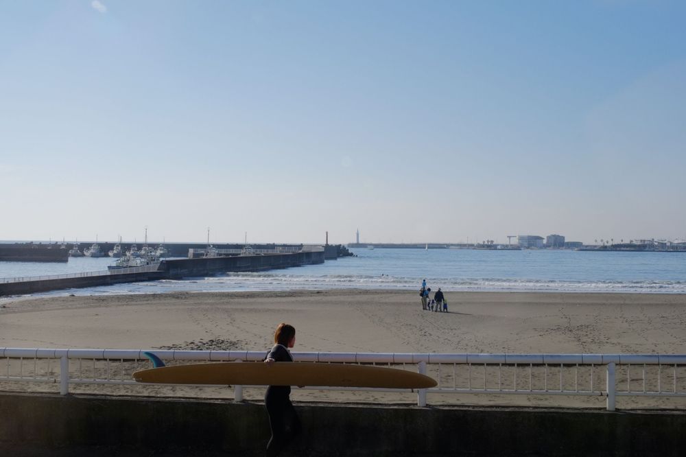 A panoramic view of a serene beach with waves rolling onto the shore and distant buildings along the coastline.