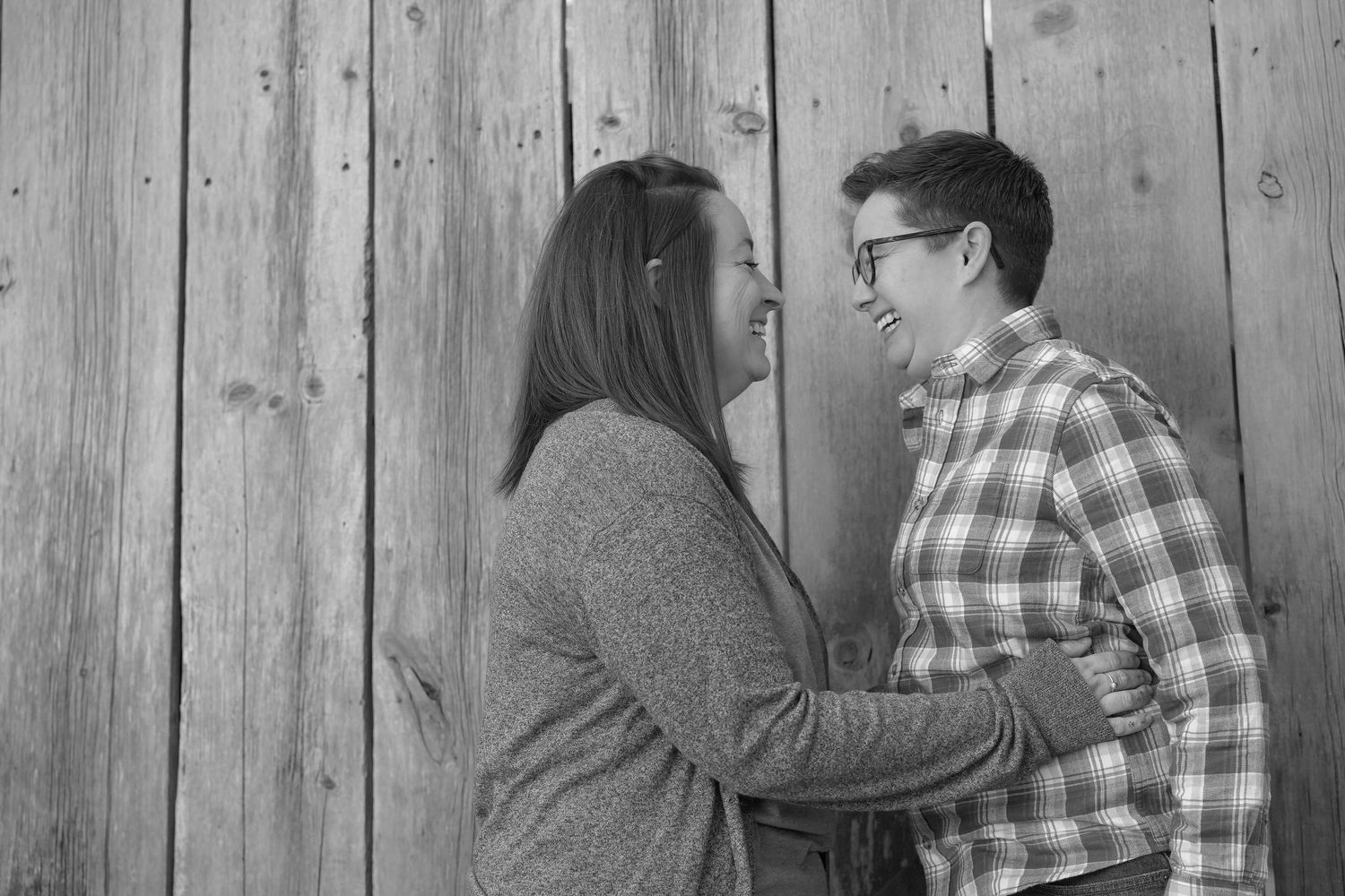 A couple shares intimate moments in a black and white photo series against a wooden fence backdrop.
