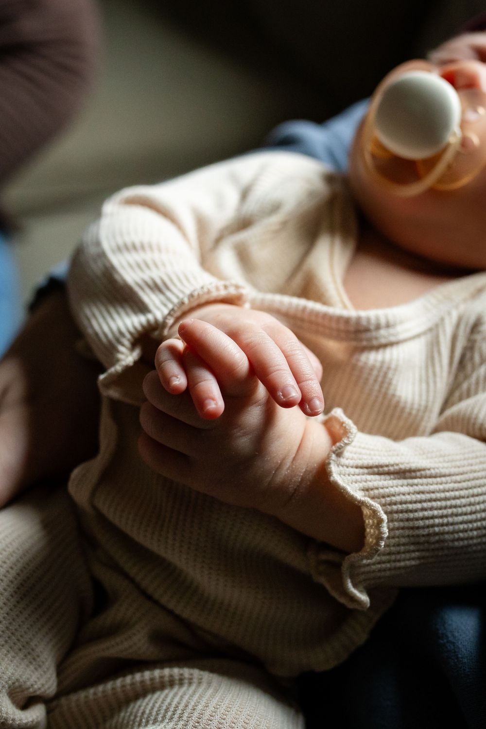 Close up of tiny baby hands resting on soft cream colored knit fabric in natural lighting.