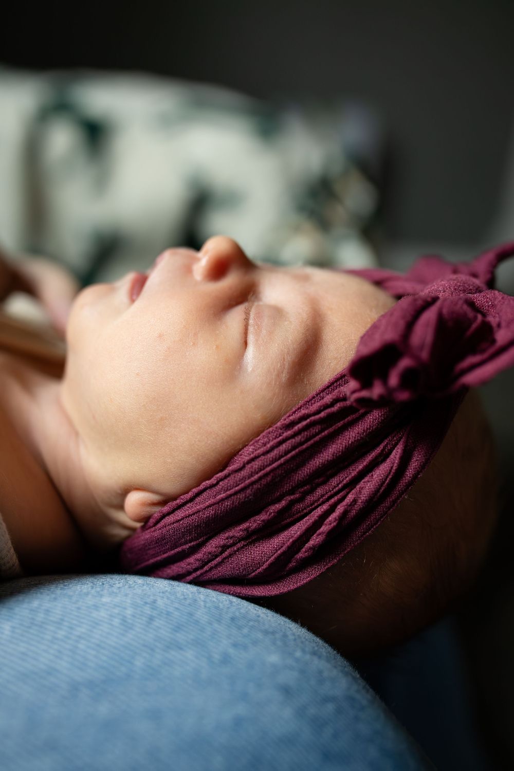 A person rests peacefully with eyes closed against a blue fabric surface while wearing a burgundy headwrap.