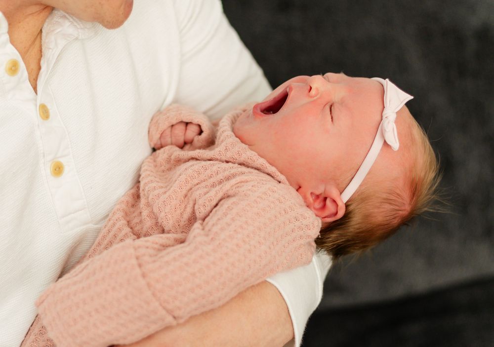 Newborn baby resting in soft peach colored wrap against dark background.