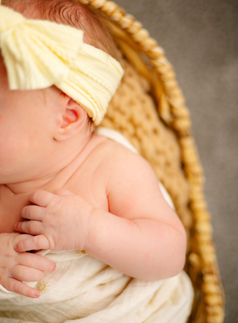 Close-up of sleeping newborn in cream wrap and basket setting.