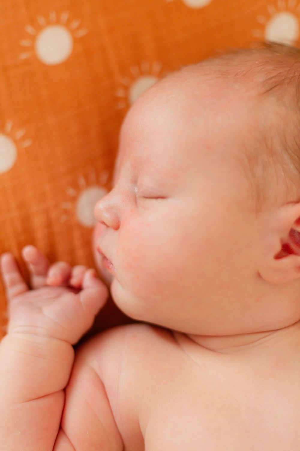 Close-up details of sleeping newborn baby against orange polka dot backdrop.