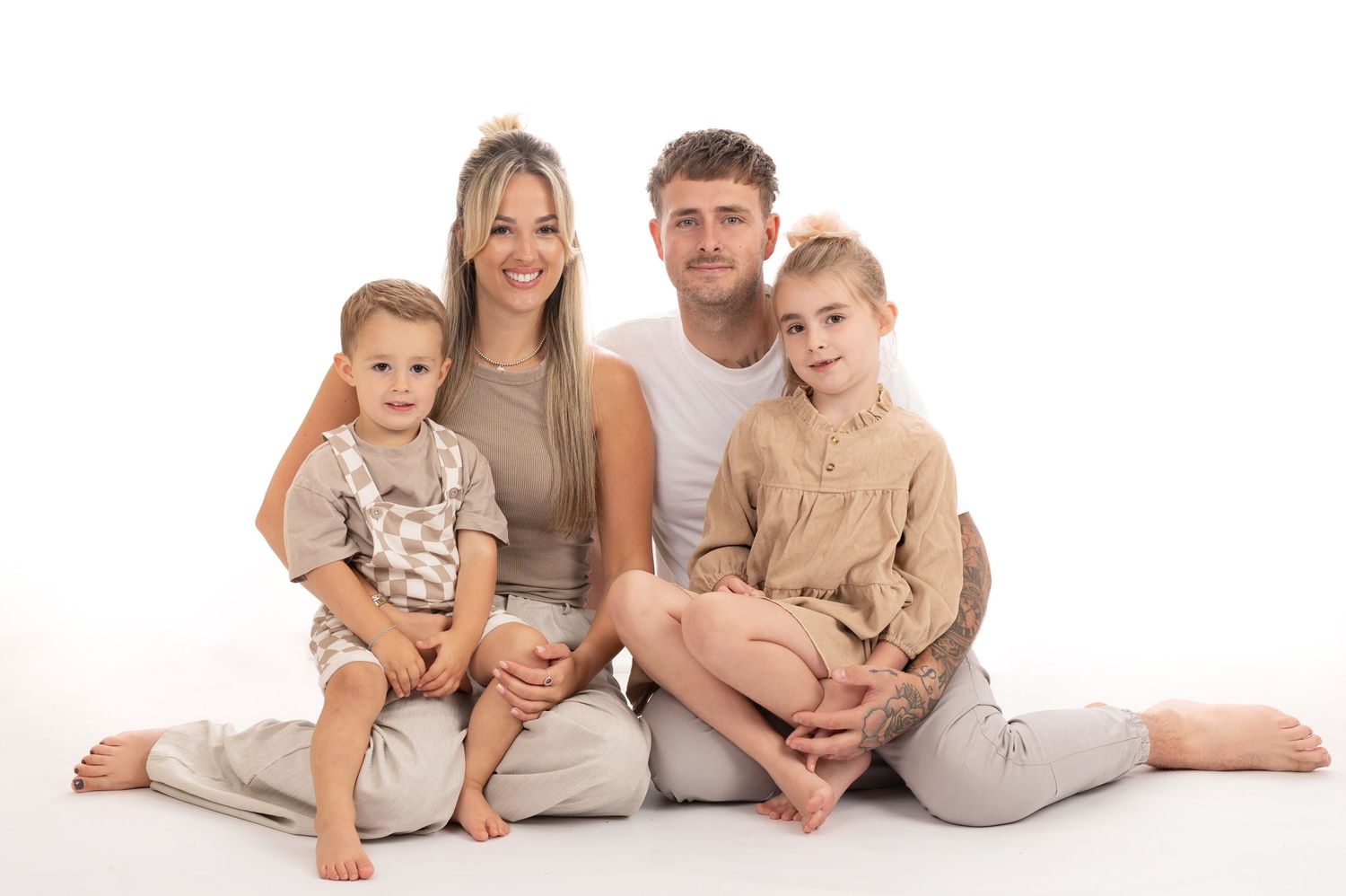 Family wearing neutral beige and white outfits poses together on white background in studio setting.