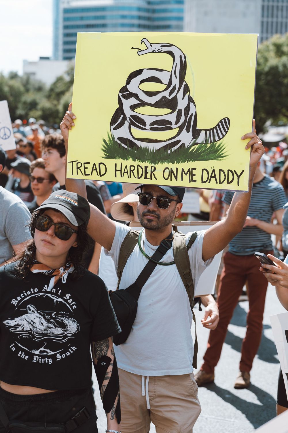 Protest marcher holds a humorous Gadsden Flag parody sign reading Tread Harder On Me Daddy.