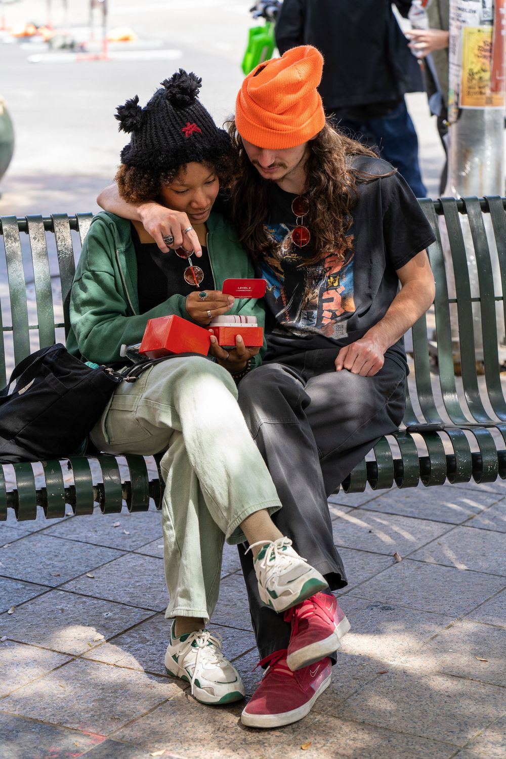 Young couple in colorful streetwear sit close together on a bench sharing a moment outdoors.