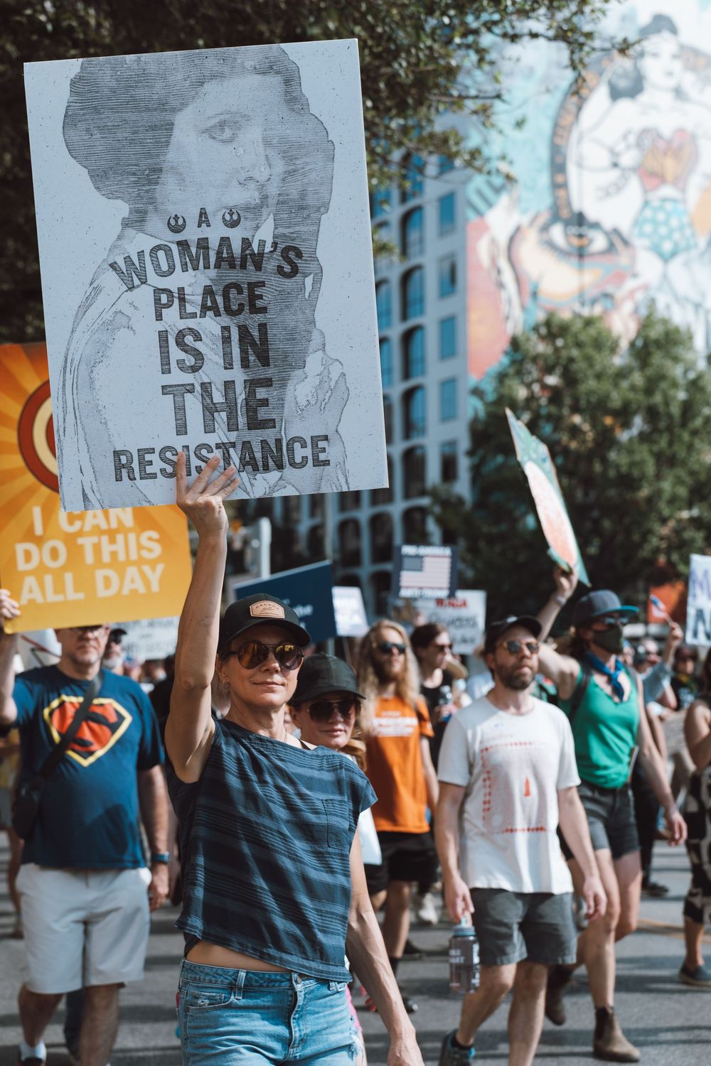 Woman marches holding a sign reading A Womans Place Is In The Resistance at a street protest.