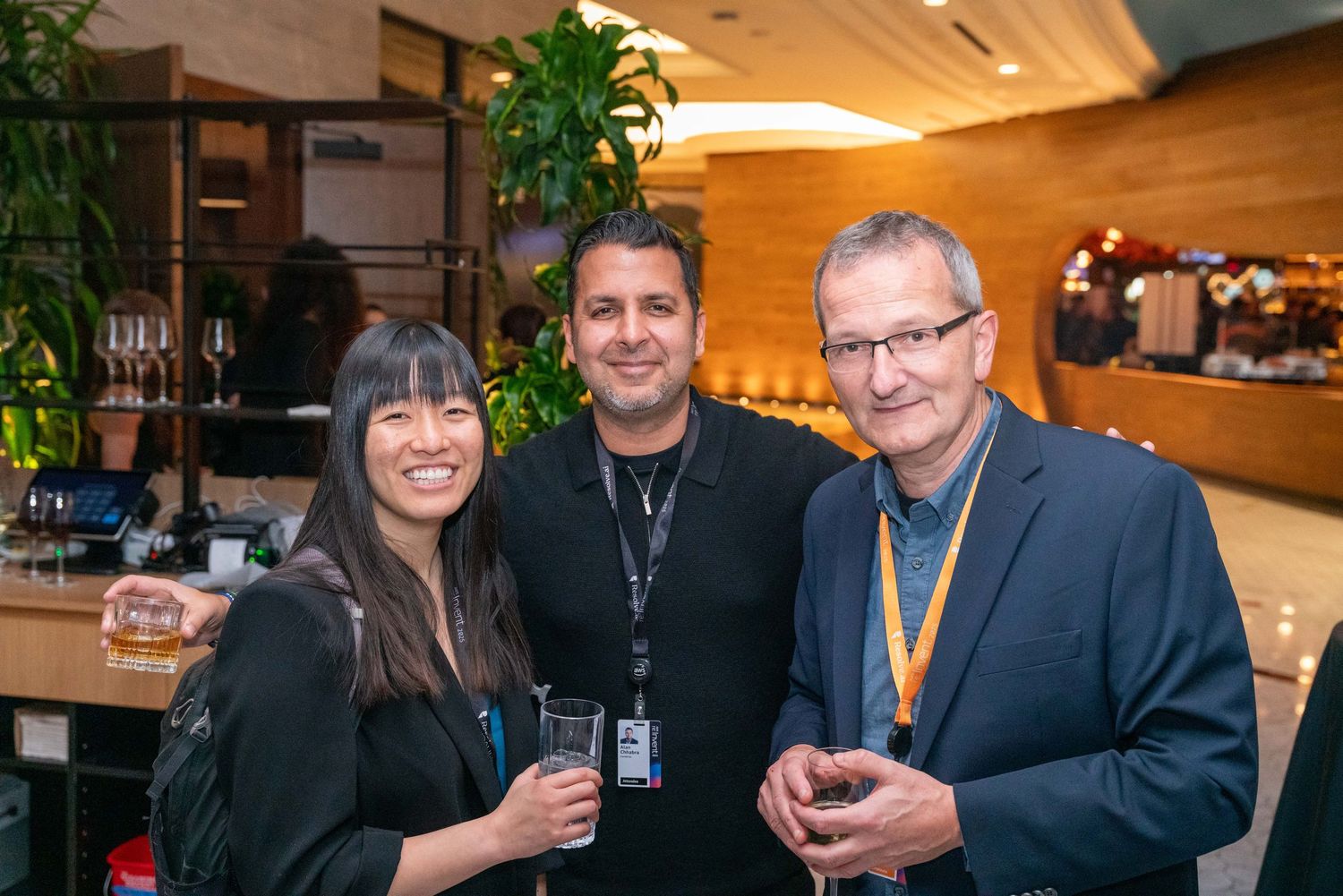 Business professionals network and socialize at a corporate event in a warmly lit wood-paneled venue.