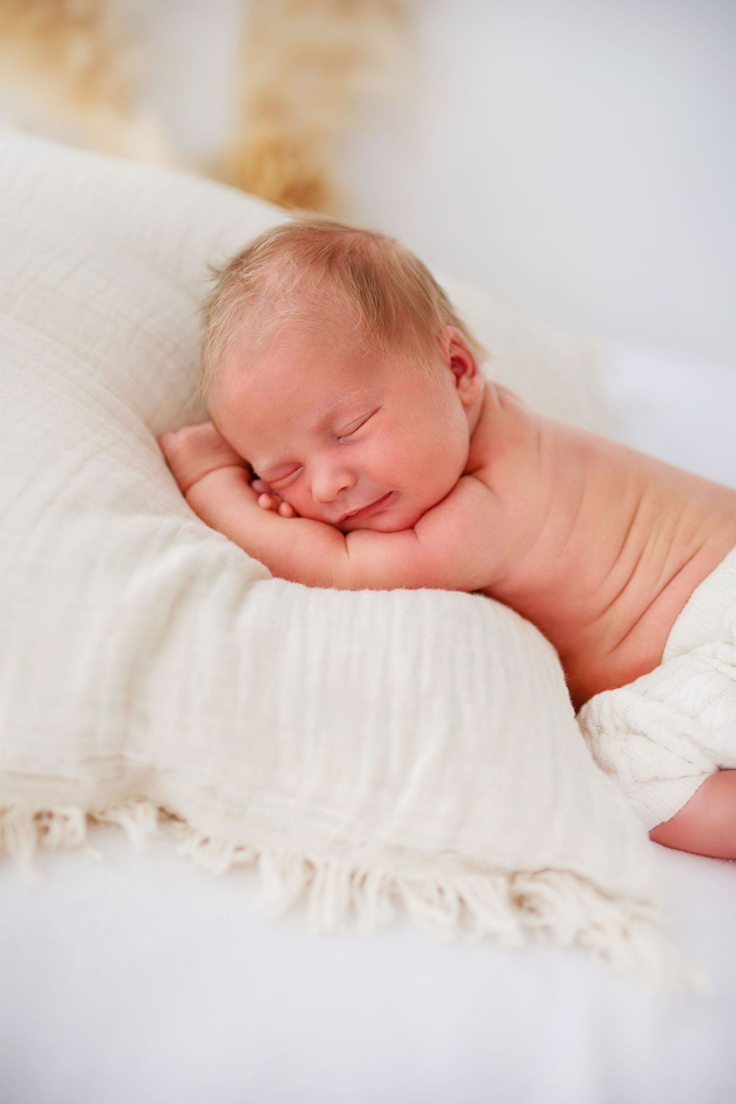 Fridfull sovande baby vilar på mjuk vit filt med naturlig belysning under sin Nyföddfotografering i Skåne