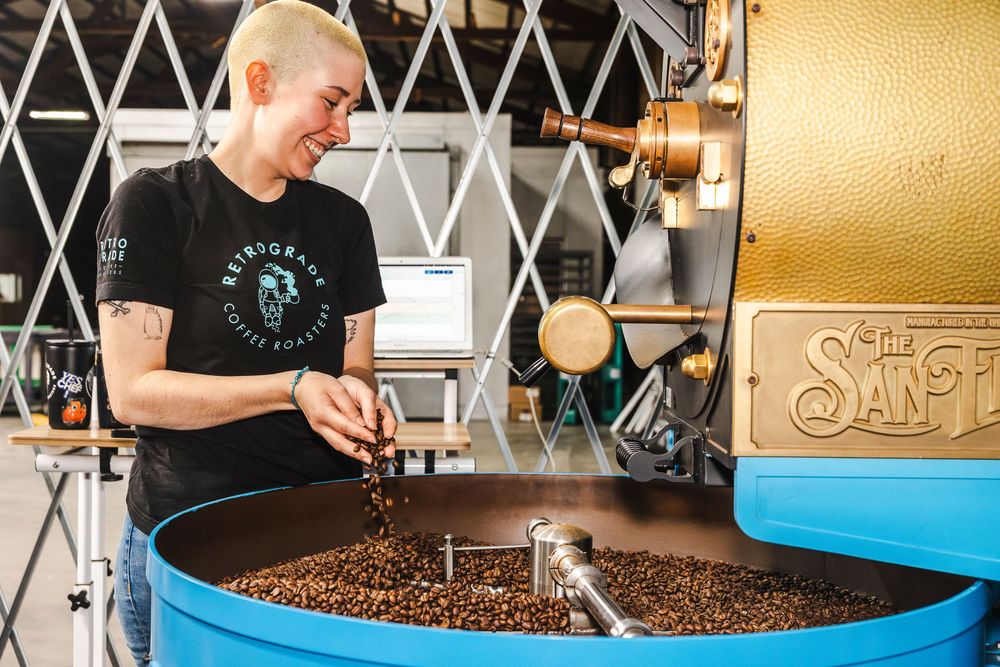 Coffee roaster examining freshly roasted beans in a large cooling tray at an artisanal roasting facility.