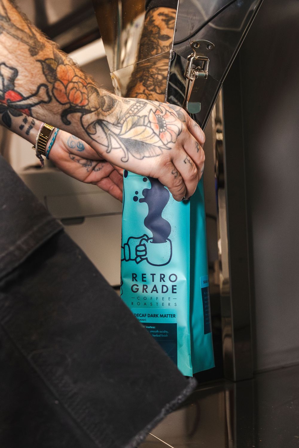 A tattooed hand holds a bright turquoise Top Grade Cannabis branded product tag against a dark background.
