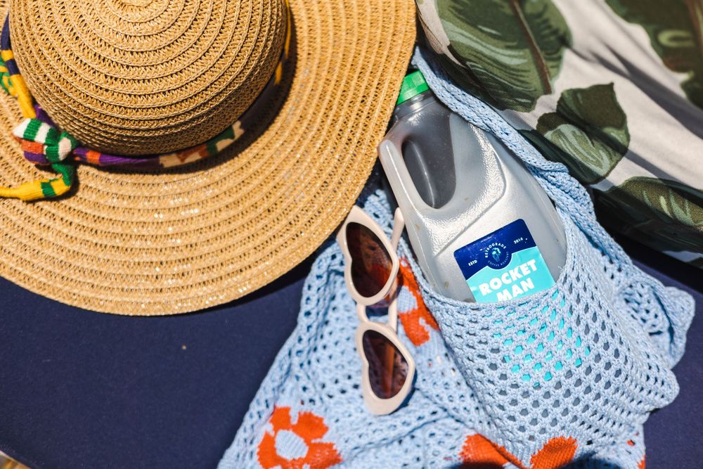 Straw hat and blue mesh swimsuit laid out with colorful beach accessories and sunscreen products.