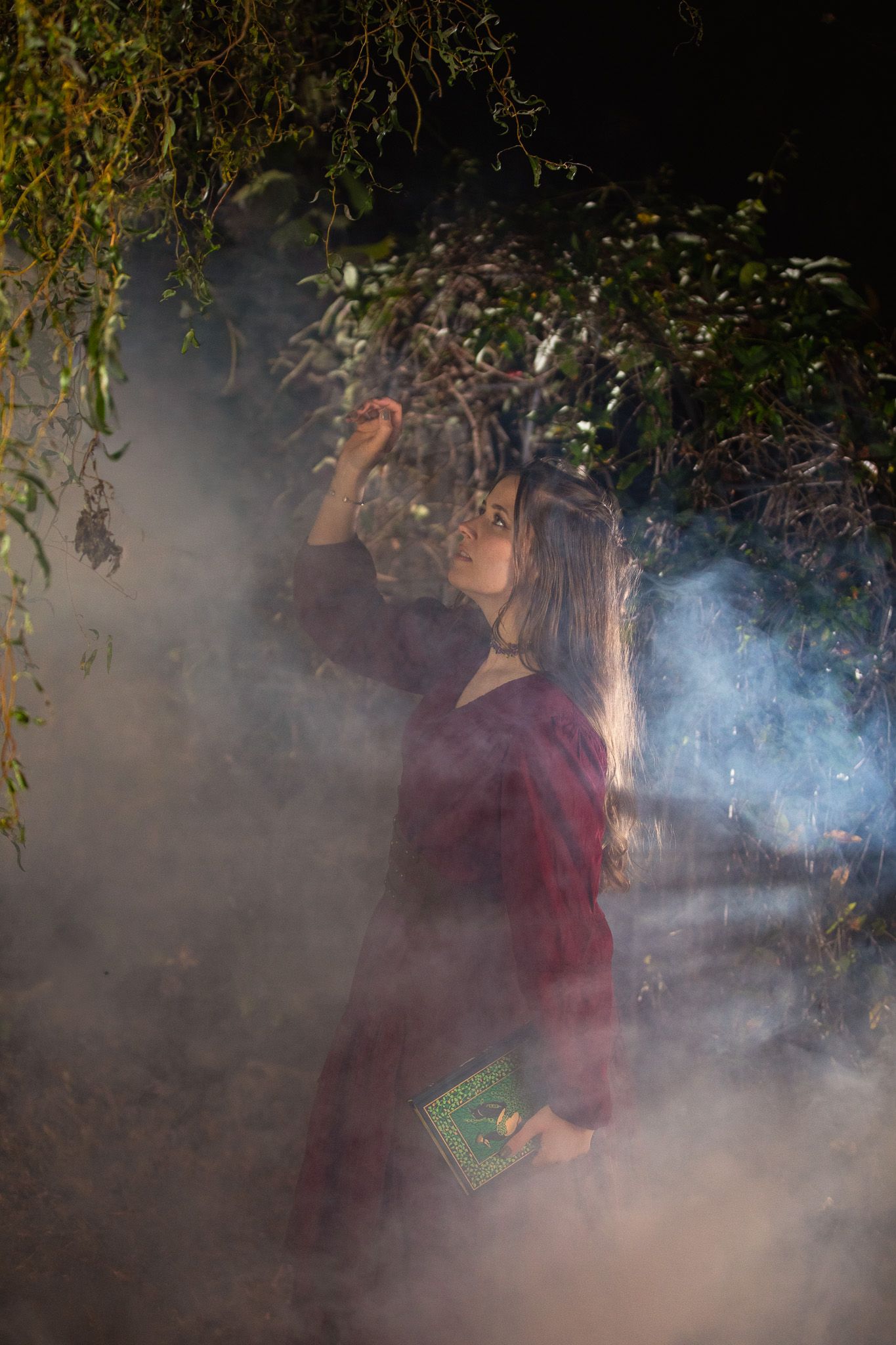 A woman drifting through tree branches with book in hand through a foggy garden.