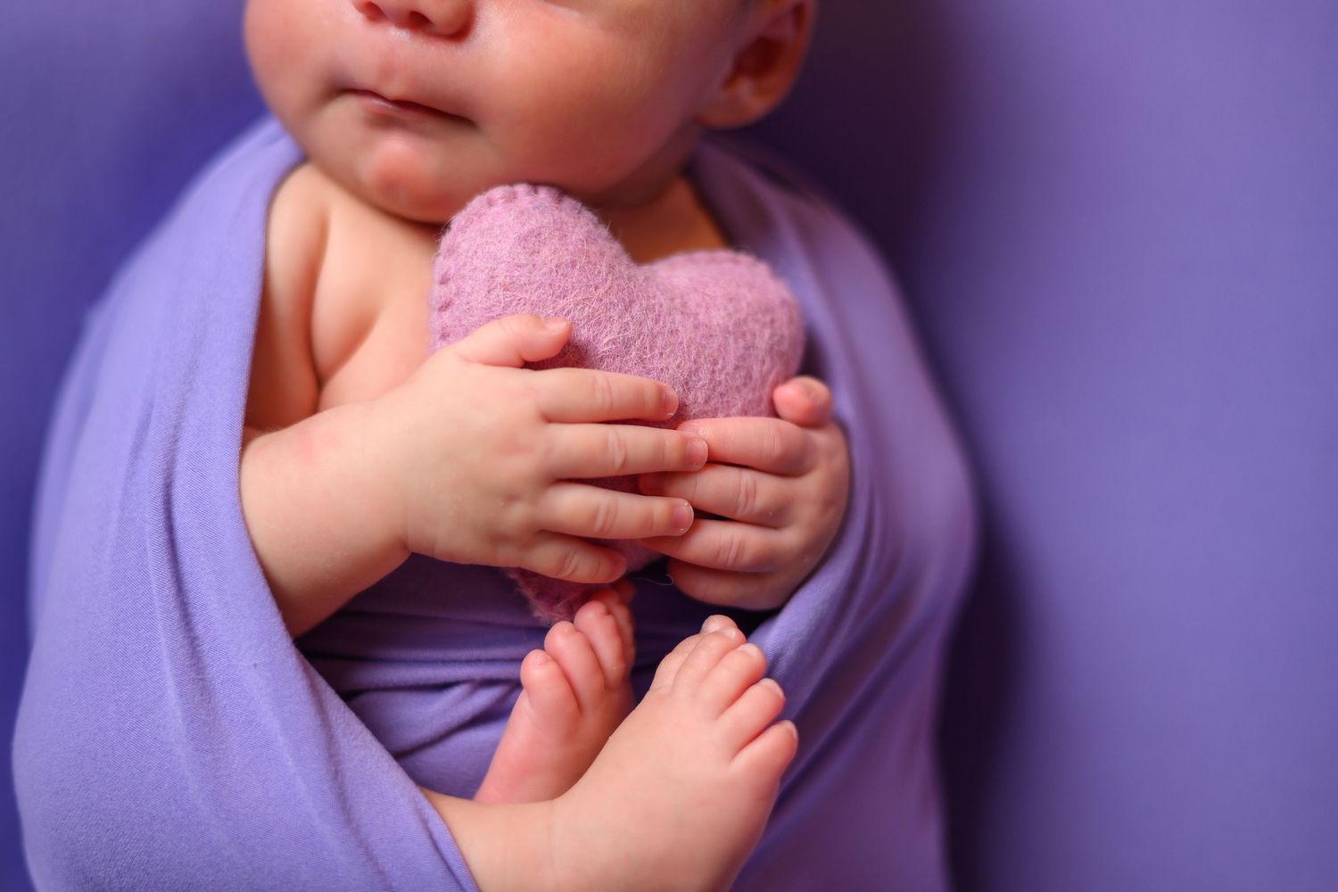 A baby in a pink bow sits in a white wooden box with fluffy pink bedding and delicate roses as decorative accents.