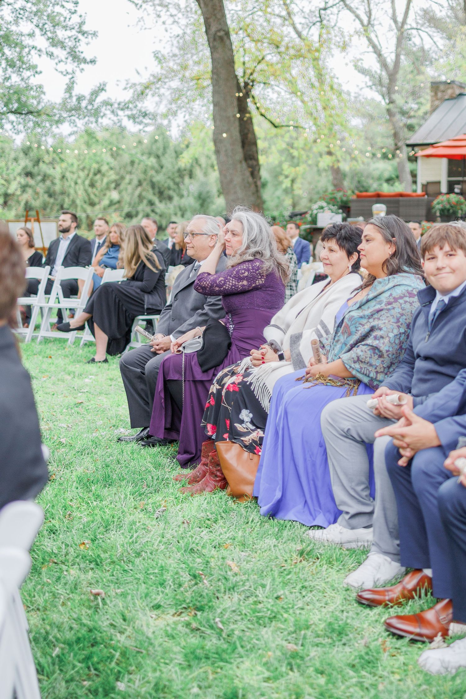 Wedding guests seated on chairs arranged on a grassy lawn during an outdoor ceremony.