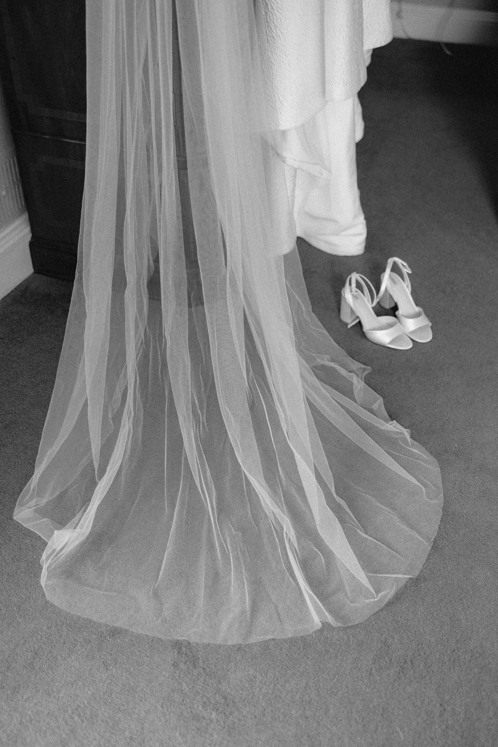 A flowing white wedding dress train with delicate tulle fabric drapes elegantly beside a pair of white bridal shoes.