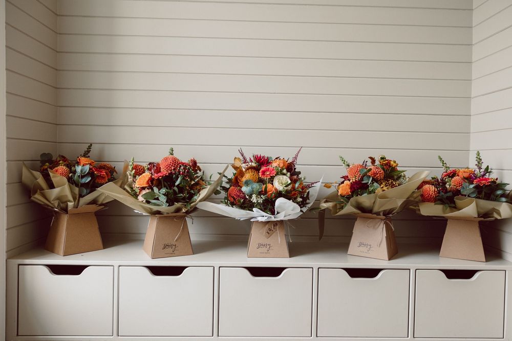 A row of brown paper wrapped floral bouquets with orange and red flowers displayed on top of white storage drawers.