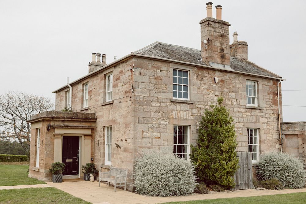 Historic stone manor house with multiple chimneys and traditional Georgian windows set against a cloudy sky.