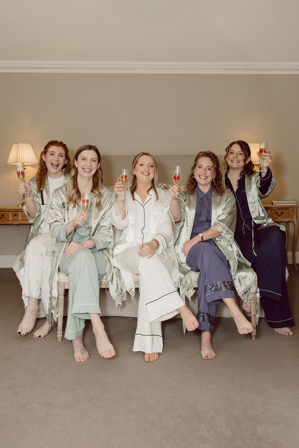 A group of friends in matching pajamas sit together on a carpeted floor showing off their feet during a sleepover party.