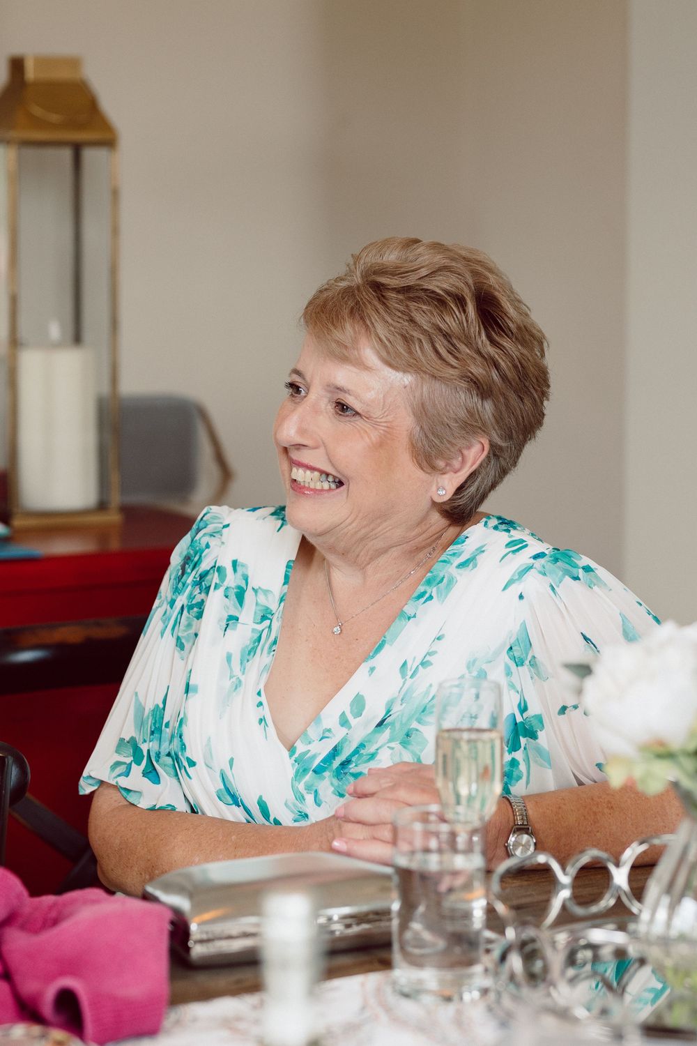 A sequence of four photos showing a person in a turquoise and white floral top laughing while seated at a dining table.