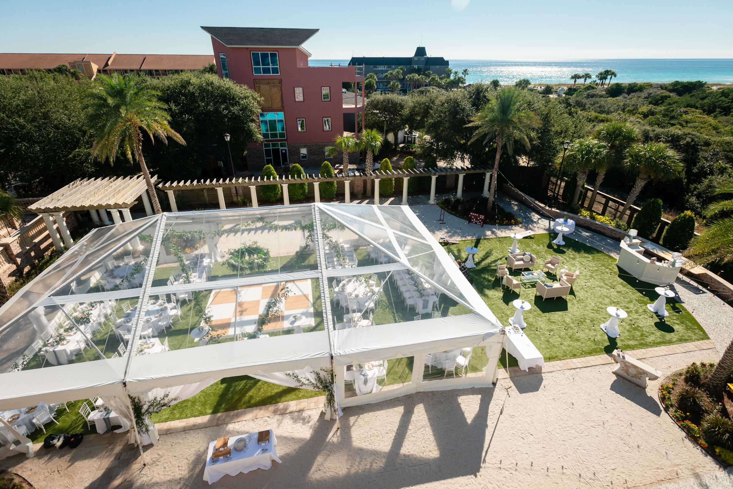 Clear tent setup for outdoor wedding reception with ocean view and palm trees.