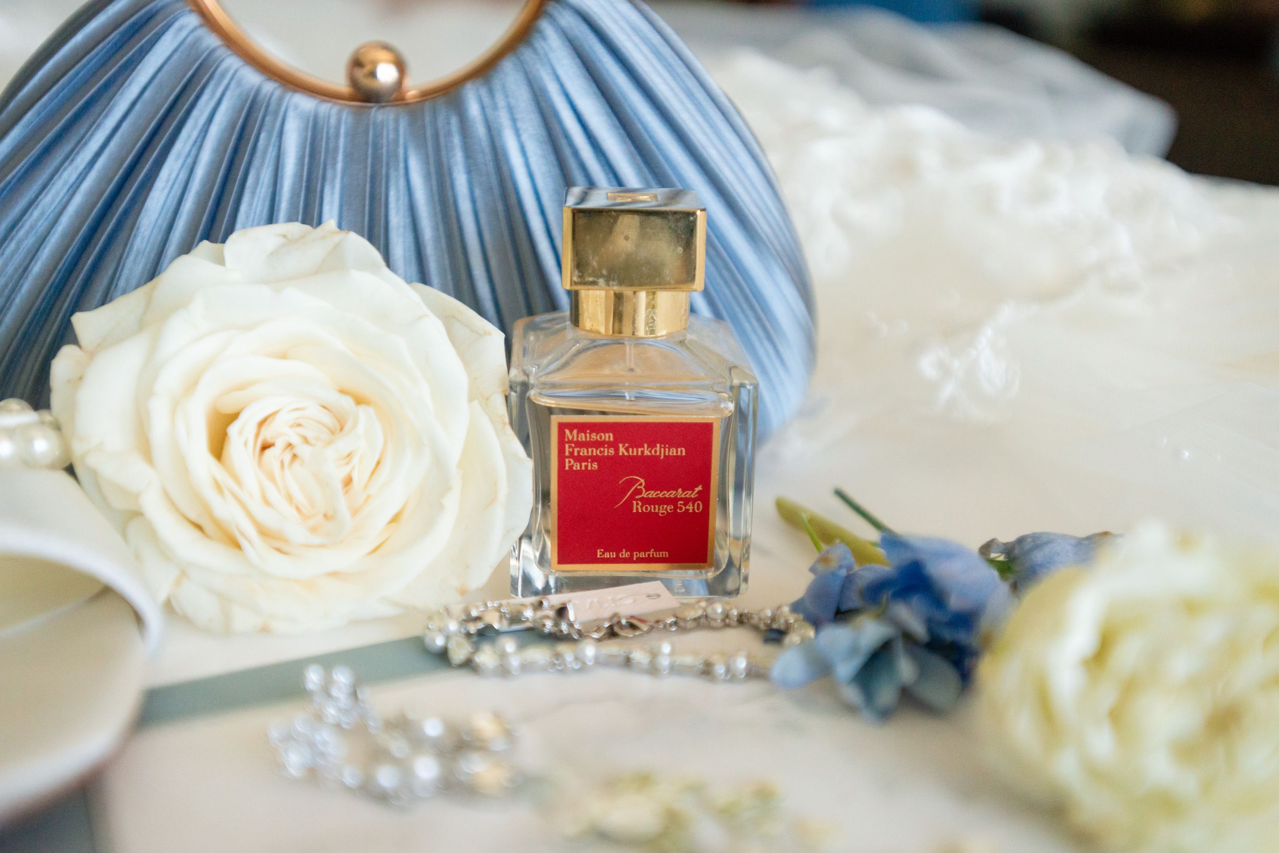 Elegant perfume bottle and white roses arranged with pearls and blue decor on a light surface.