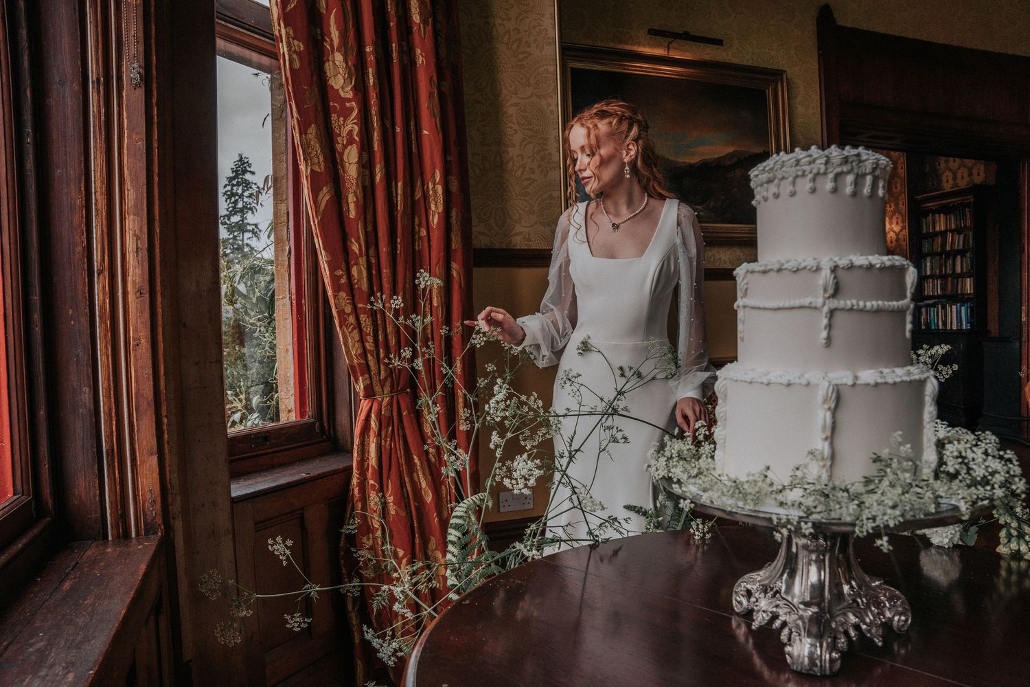 Bride standing beside a three tier white wedding cake with royal icing details at Huntsham Court wedding venue