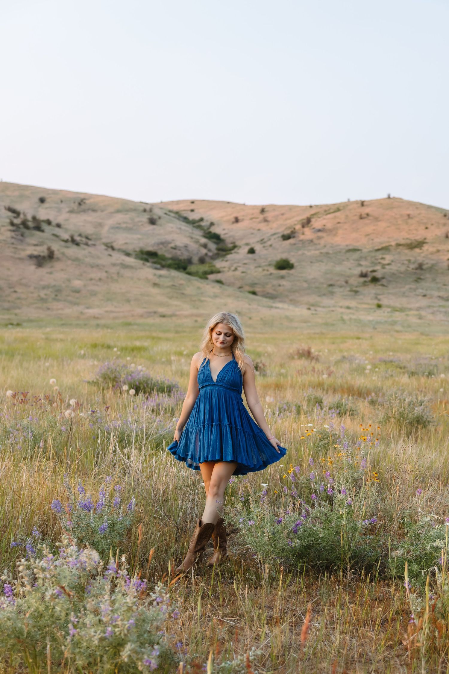 A flowing blue dress twirls among vibrant wildflowers in a golden meadow with rolling hills in the background.
