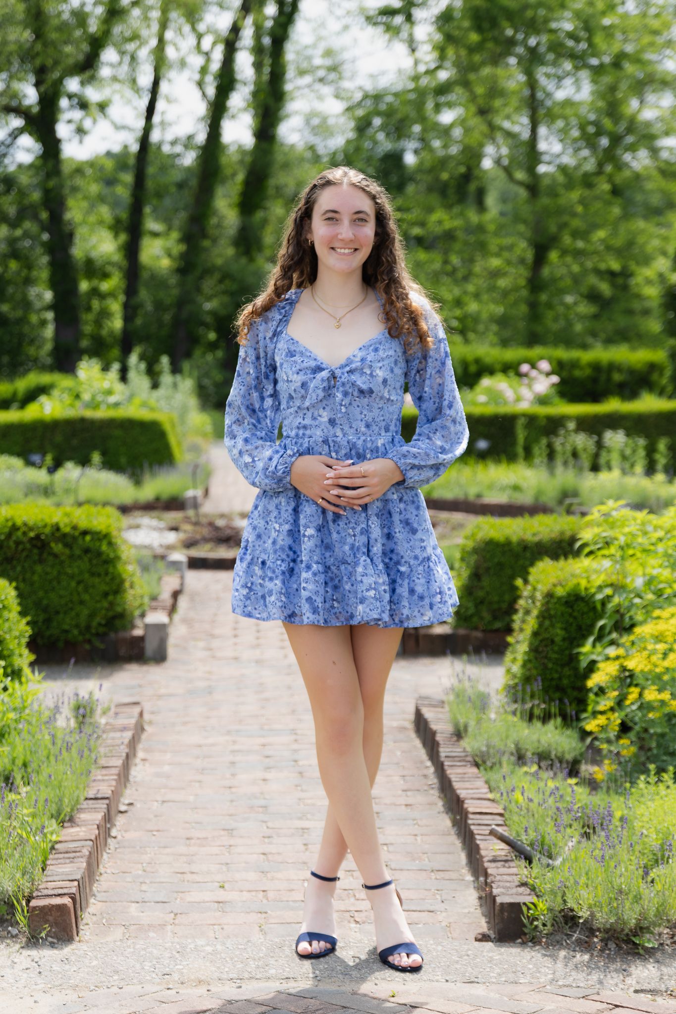 High school senior girl is smiling in a blue dress for her senior photos at Matthaei Botanical Gardens in Ann Arbor.