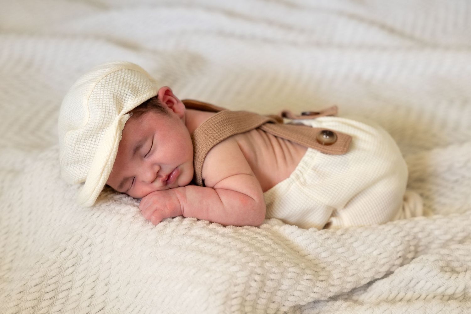 A newborn baby sleeps peacefully on a textured white blanket in a serene nursery setting.