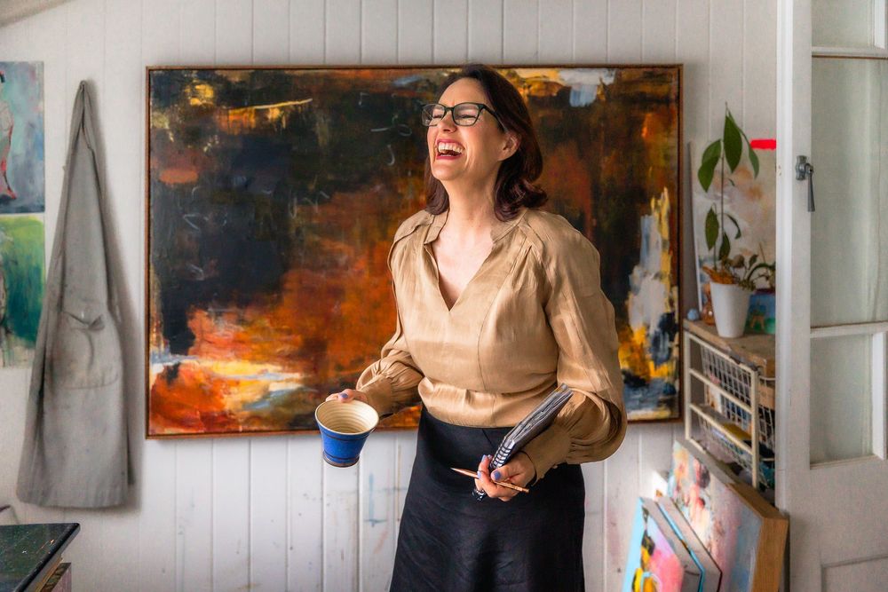 Artist working in a bright studio space surrounded by colorful abstract paintings and creative materials.