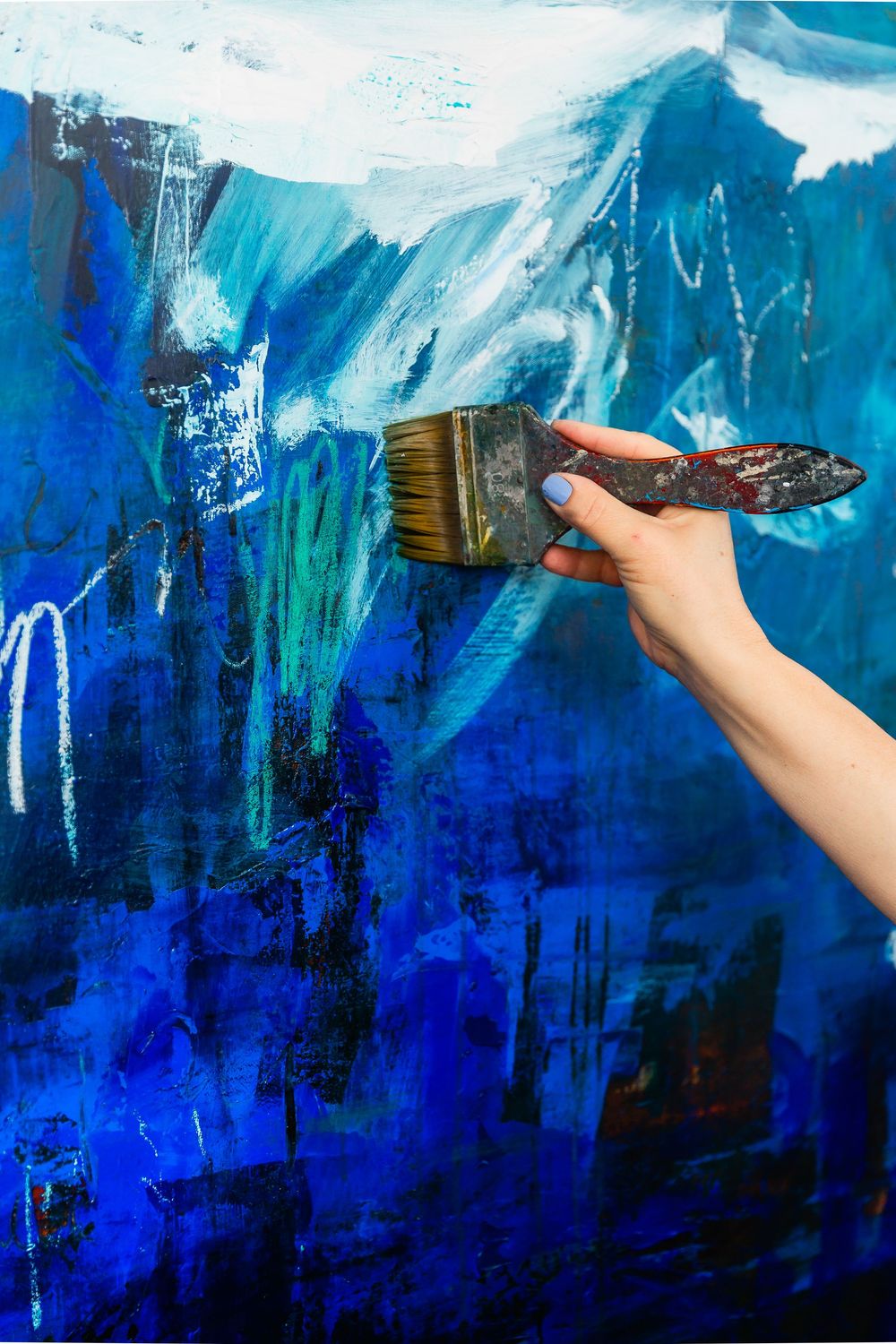 Hand with paintbrush creating abstract art in vibrant shades of blue.