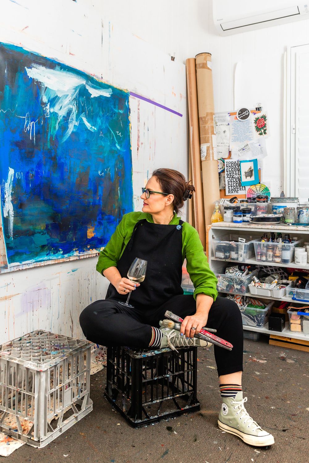 Artist relaxing in studio with blue artwork and wine glass.